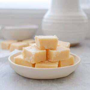 Slices of Vanilla Fudge stacked up on a small white serving dish which is sitting on a bench.