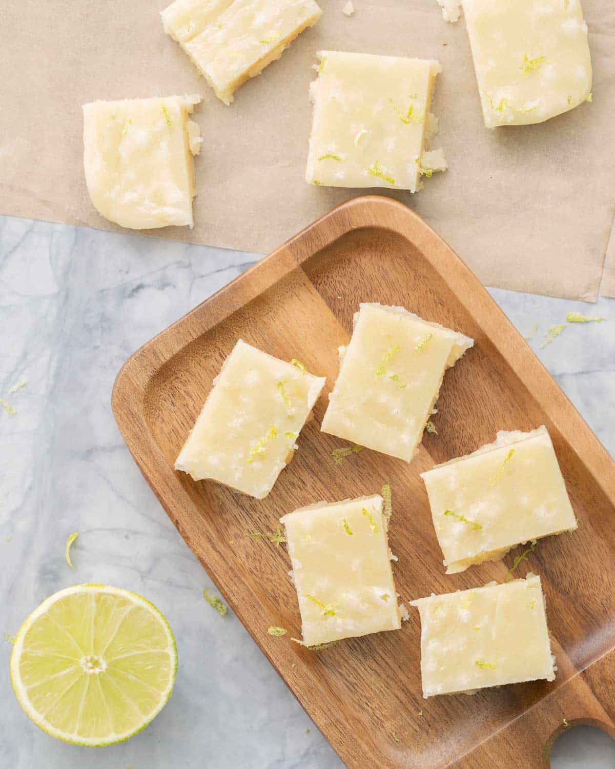 Slices of vegan fudge resting on baking paper and a wooden serving board next to a lime wedge 