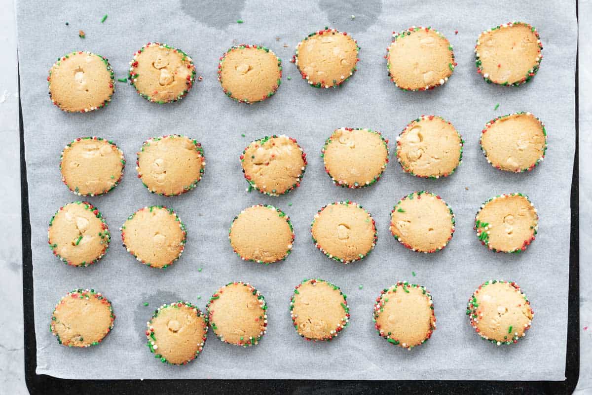 Baked Christmas sprinkle cookies resting on a lined baking tray 