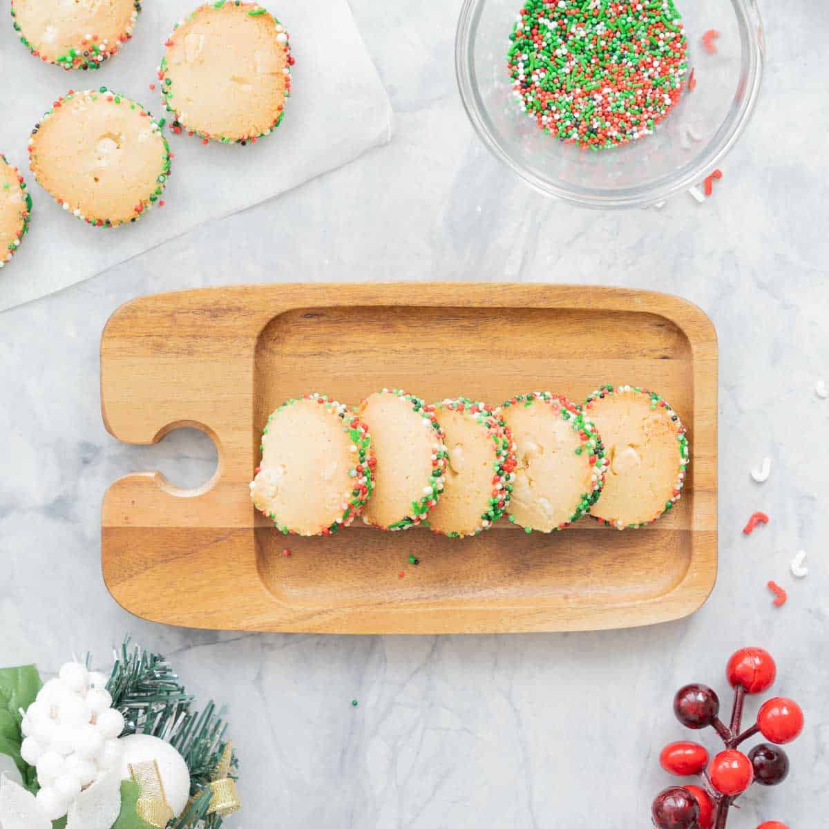 A small wooden serving platter with a row of Christmas Sprinkle Cookies below, 