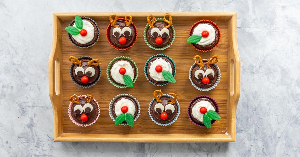 A tray of christmas cupcakes, half decorated as figgy puddings and half decorated as reindeer. 