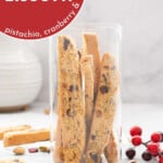 A tall glass jar fill with Christmas biscotti with text overlay for pinterest