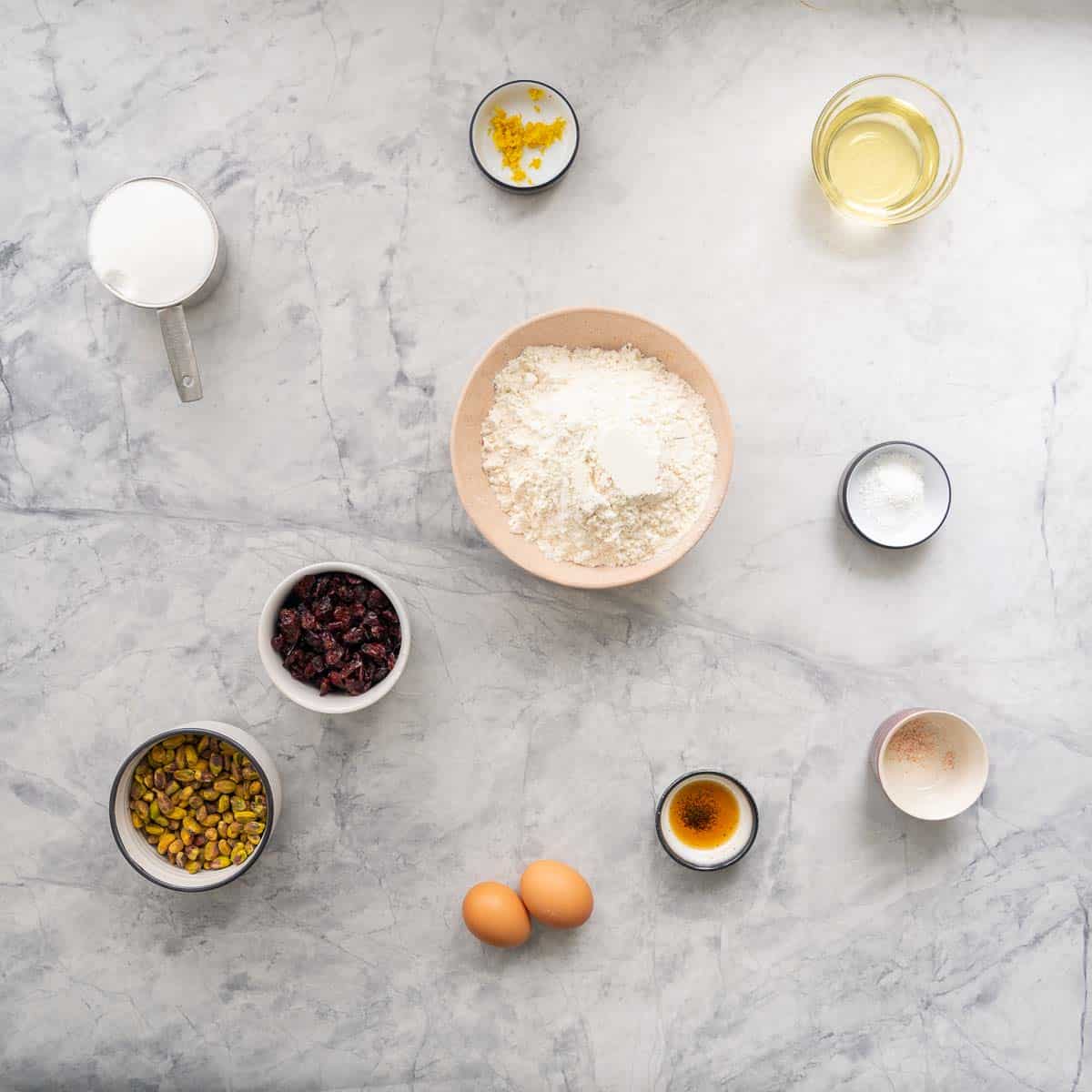 The ingredients to make cranberry pistachio biscotti laid out on a grey marble bench top.