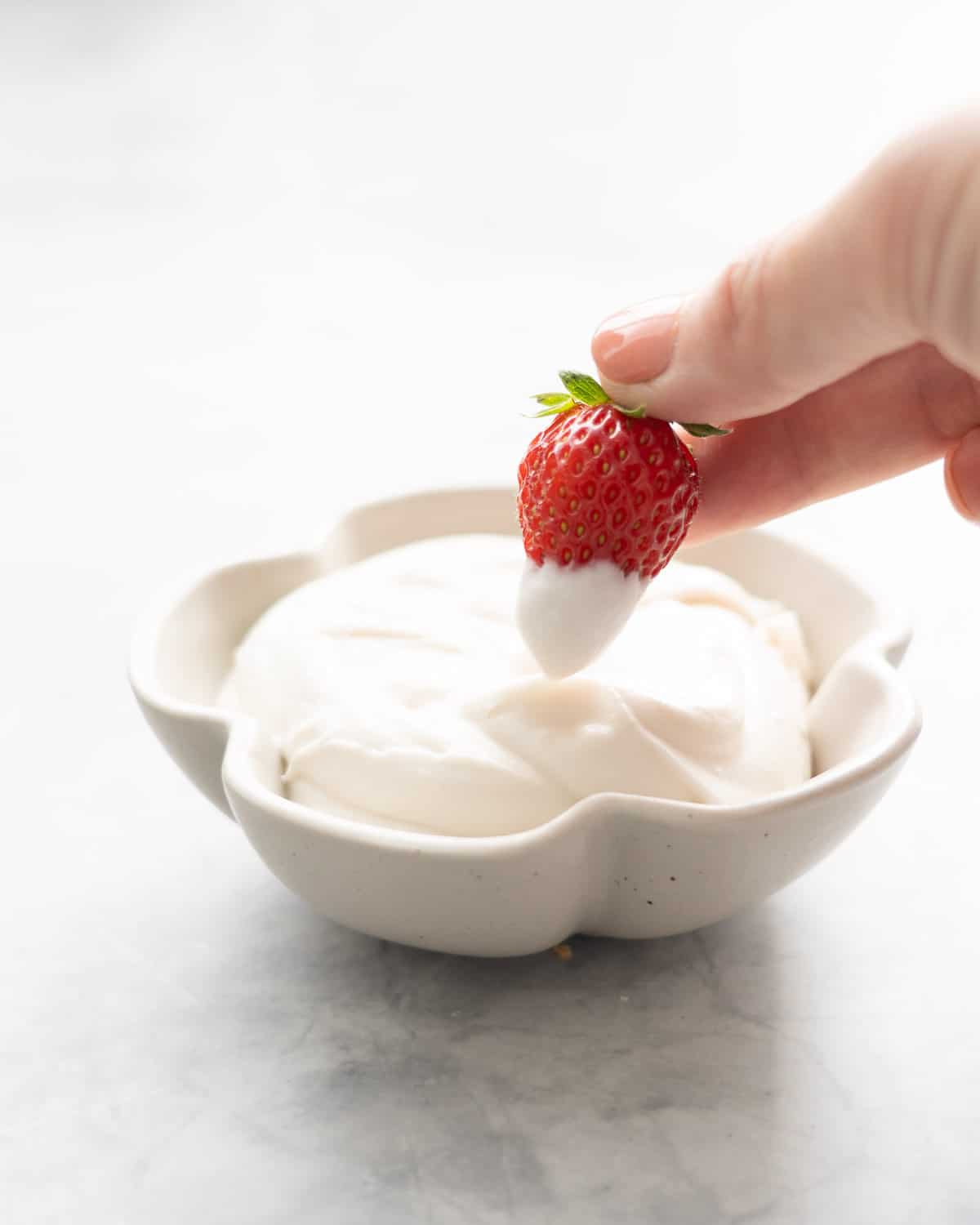 A strawberry being dipped into a small flower shaped bowl of whipped coconut cream