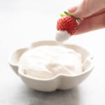 A strawberry being dipped into a small flower shaped bowl of whipped coconut cream