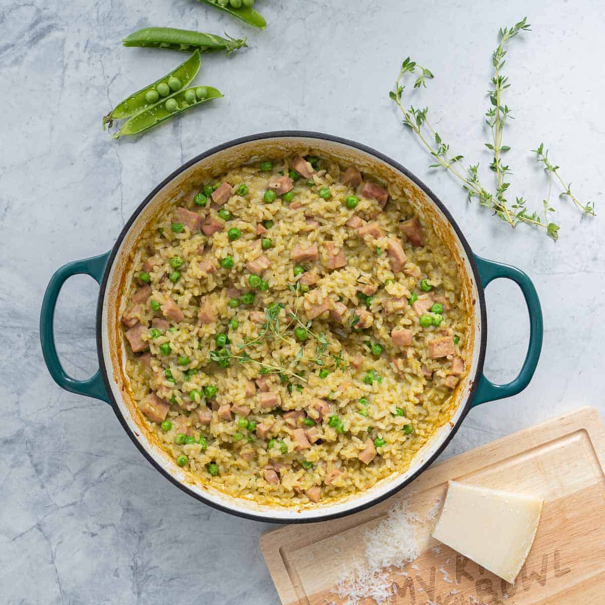 A top down shot of a large pan of pea risotto studded with chunks of pink ham
