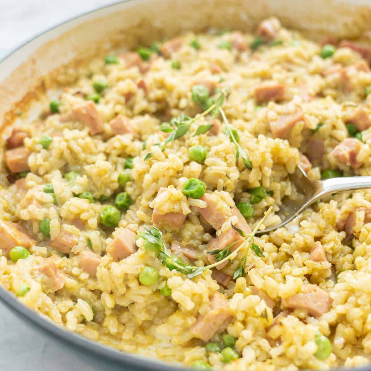 A spoonful of pea and ham being served from a pan of risotto 