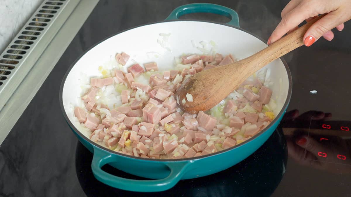 chunks of ham and diced onion sauteing in a pan