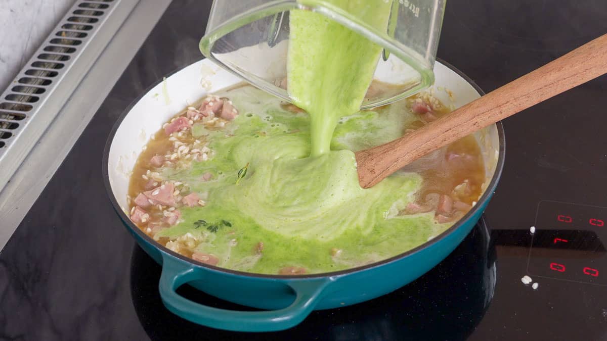 A bright green puree of peas and stock being poured into a pan of risotto