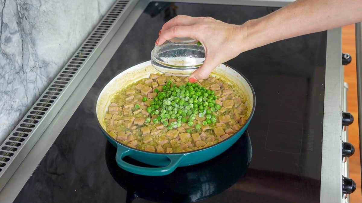 Frozen peas being added to a pan of risotto