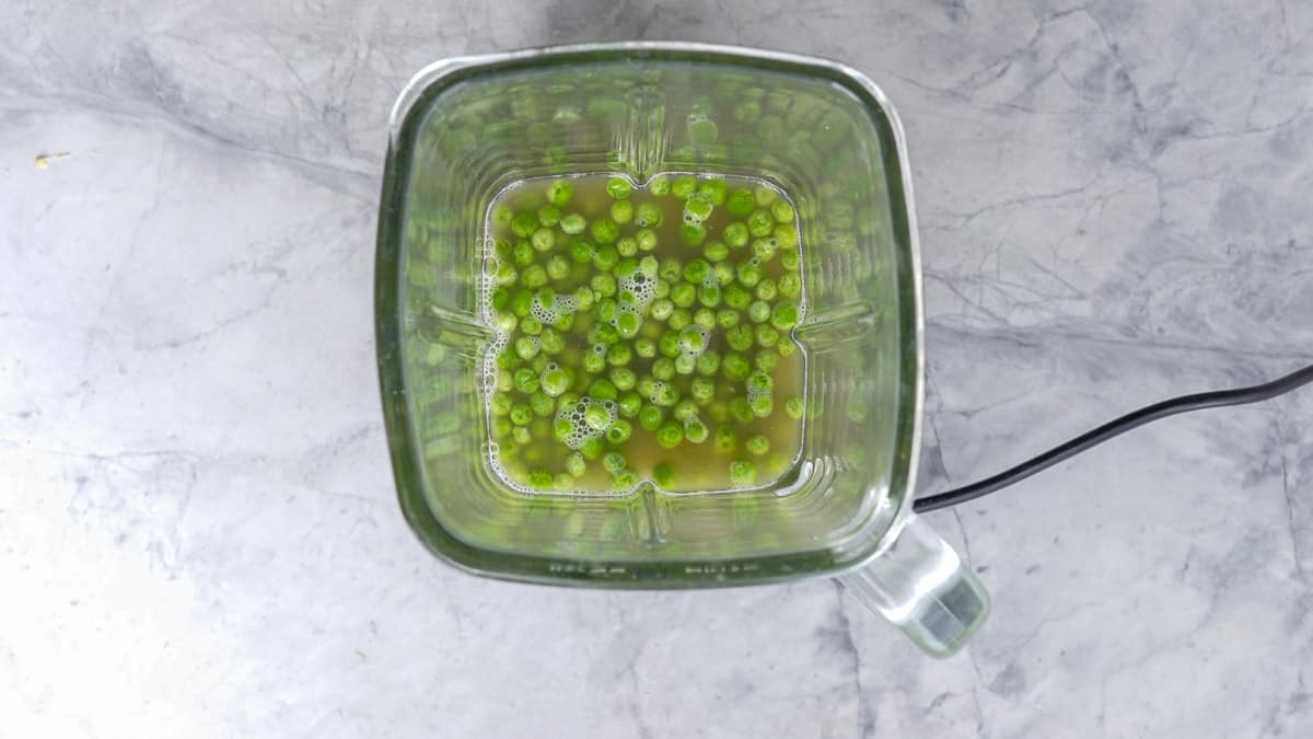 Peas floating  in stock in the glass jug of a blender. 