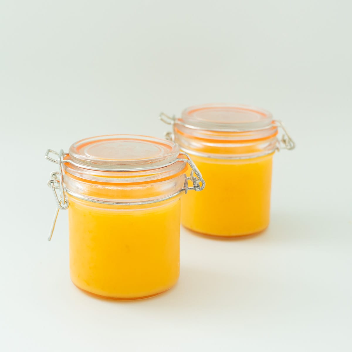 two glass jars full of lemon butter with the lids closed. 