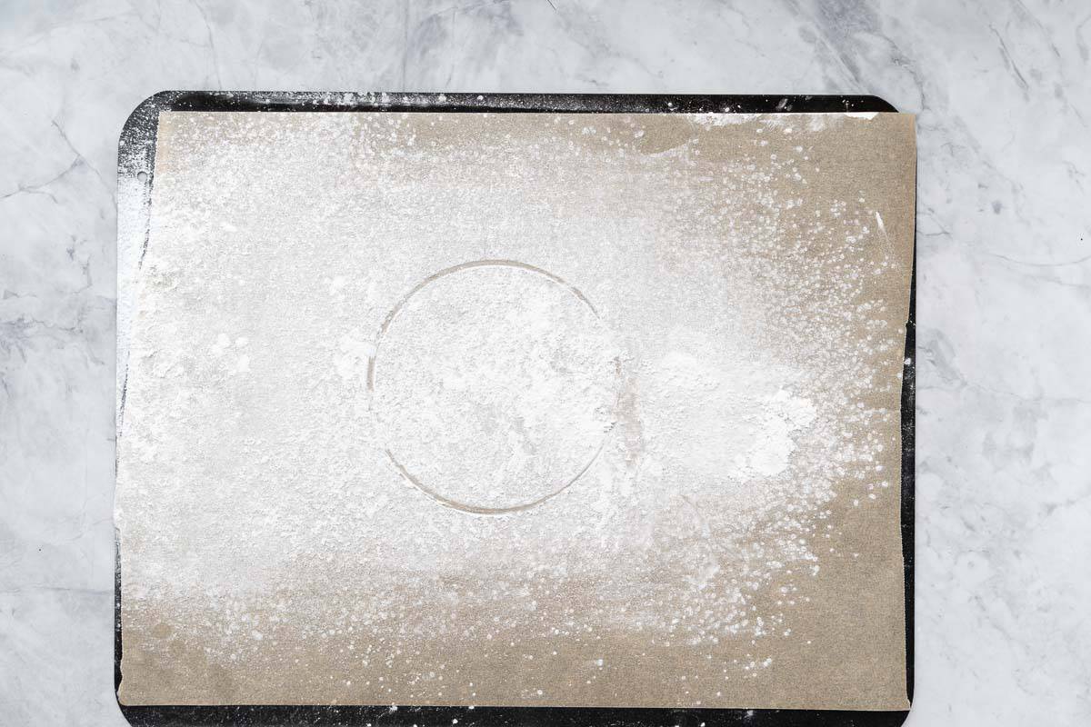 A lined baking sheet dusted with cornflour, with the outline of a mixing bowl visible in the cornflour dusting. 