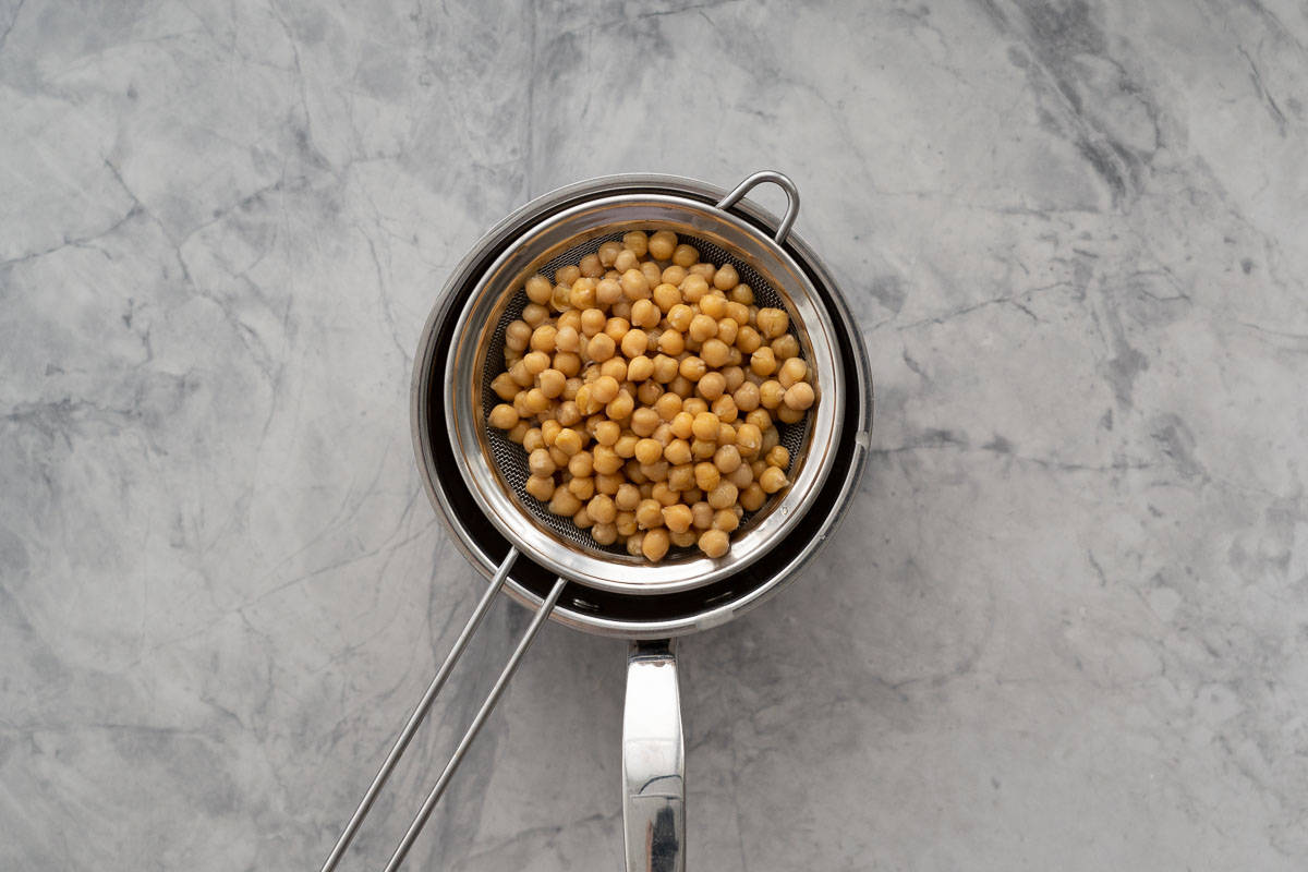 Chickpeas in a sieve resting on a stainless steel pot. 