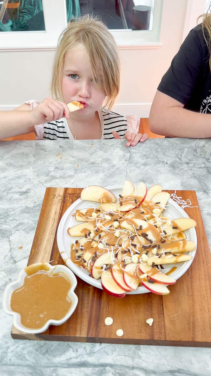 A young girl eating an apple slice drizzled in caramel sauce. 