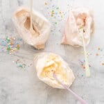 Three ziplock bags of ice cream with spoons on a marble bench scattered with sprinkles.
