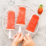 Childrens hands reaching to pick up popsicles from a bowl filled with ice.