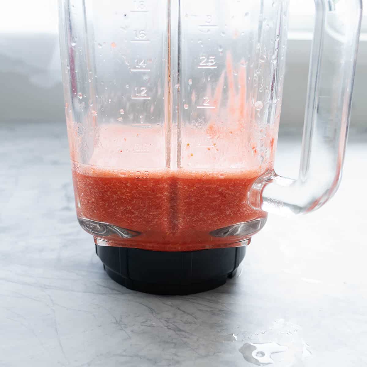 A blender jug of strawberry smoothie, a slightly chunky texture of strawberries visible. 