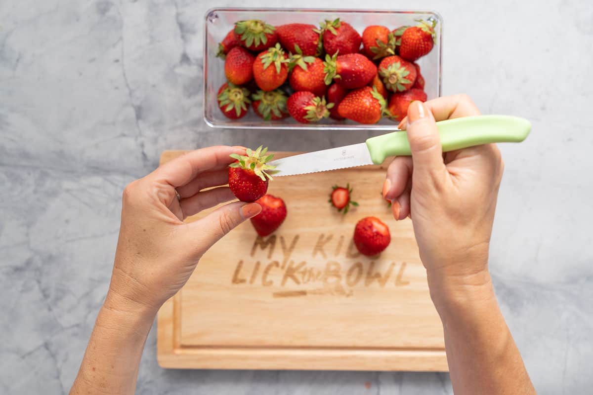 A small green fruit knife being used to hull a strawberry 