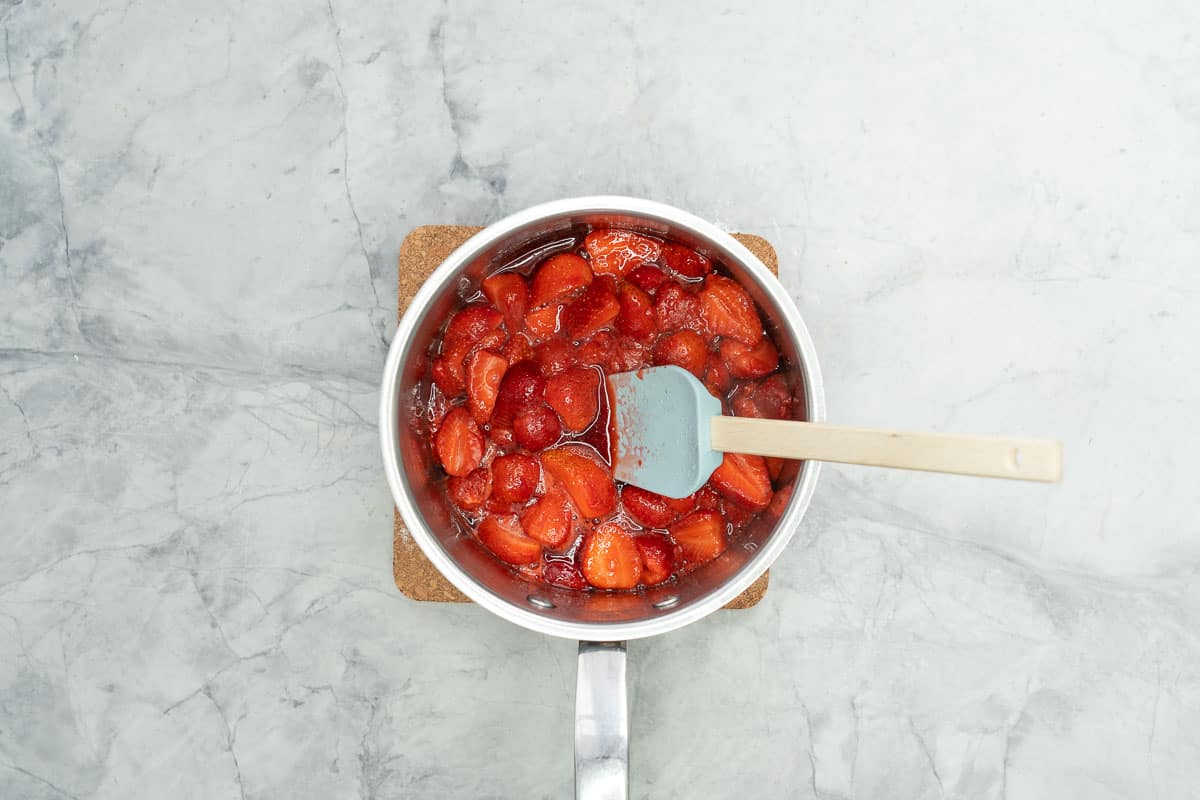 Stewed strawberries in a saucepan with a light blue spatula