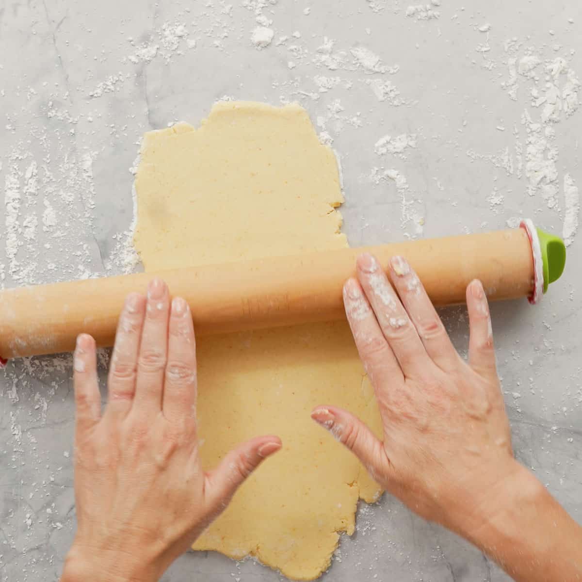 Two hands rolling a rolling out the cheese cracker dough with a rolling pin 