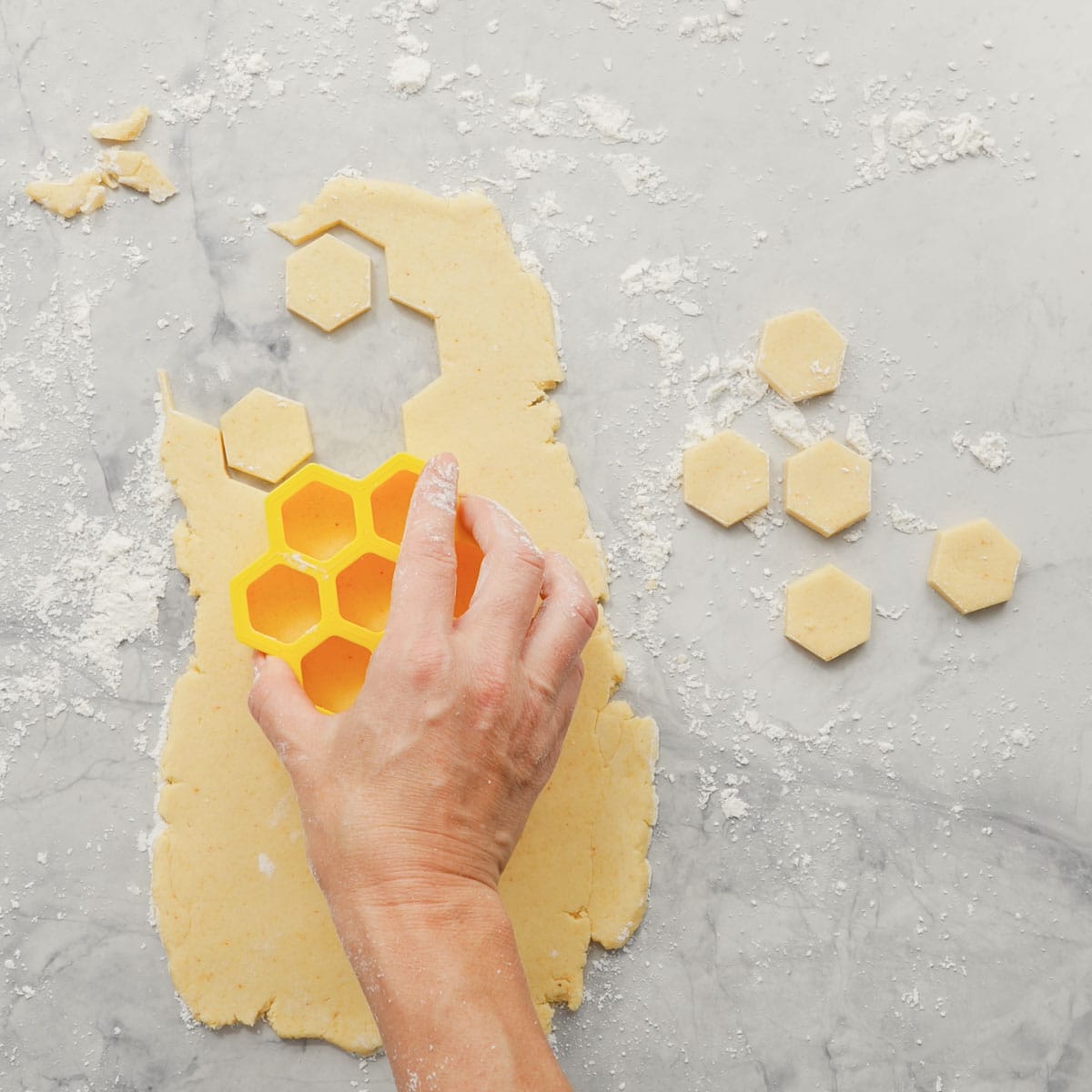 Rolled out dough on a floured surface, with a hand pressing a cutter into it to create small hexagons.  