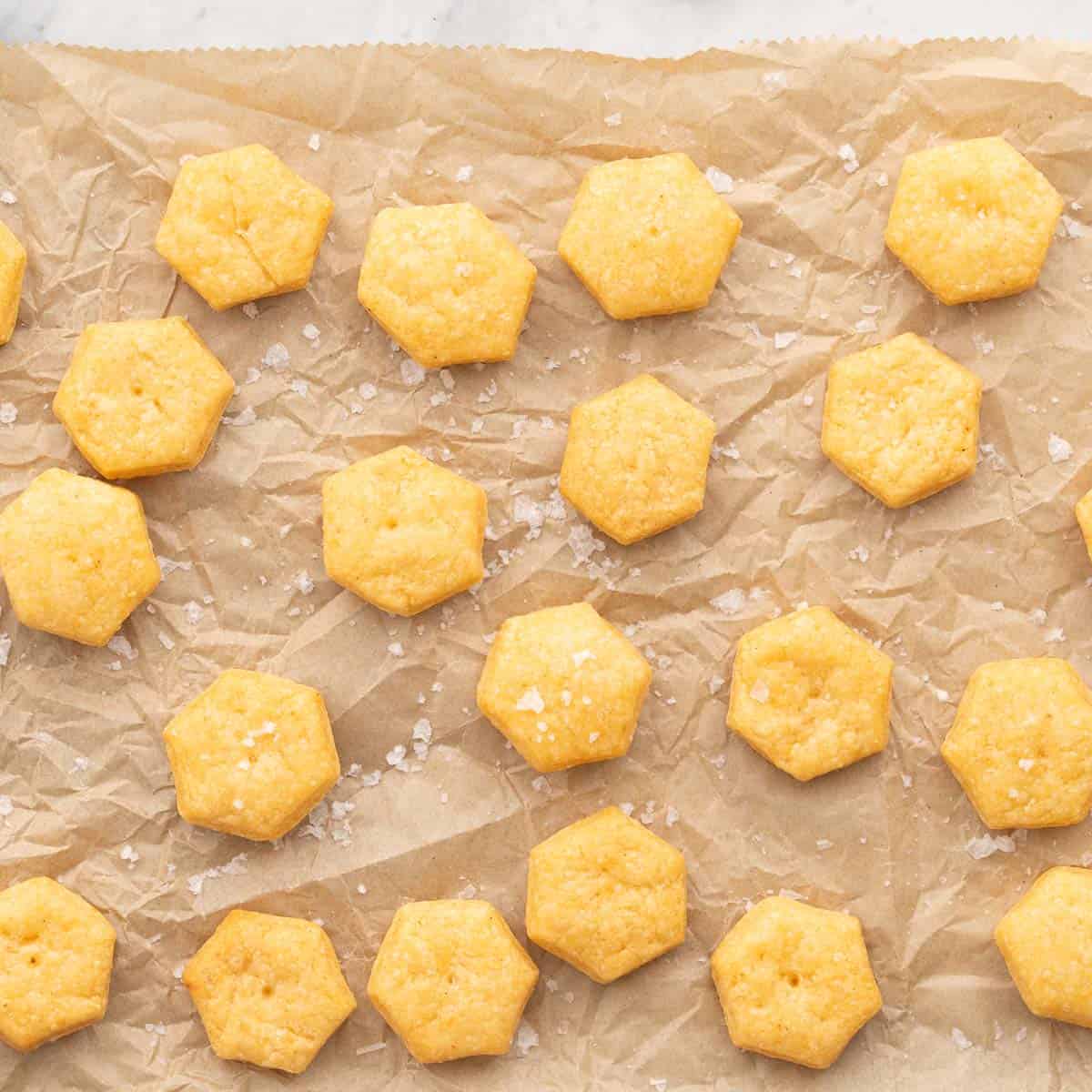 Golden brown baked cheese crackers resting on a lined baking tray with a sprinkling of sea salt on the top. 