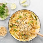 A fry pan of pad thai topped with bean sprouts, nuts and coriander leaves.
