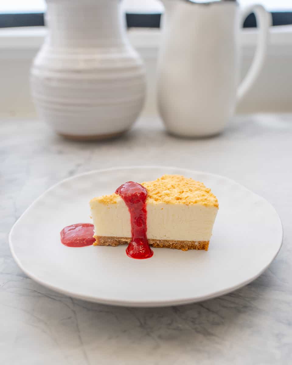 A small serving of cheesecake on a small ceramic plate,  with raspberry puree drizzled over the top 