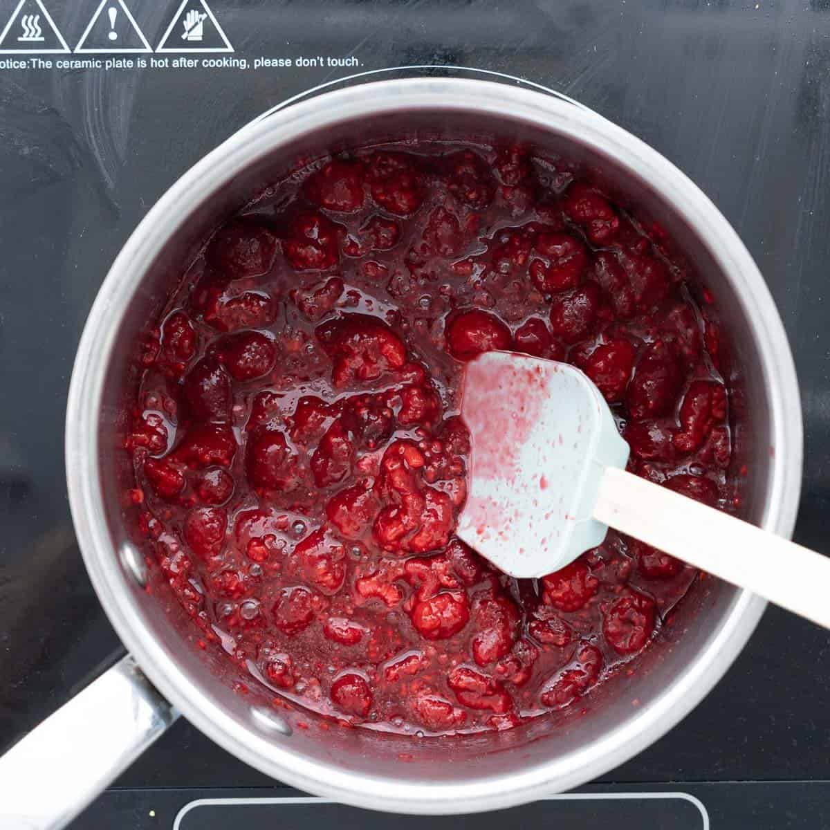 All the ingredients to make the raspberry puree in a saucepan on the element simmering with a spatula resting on the side