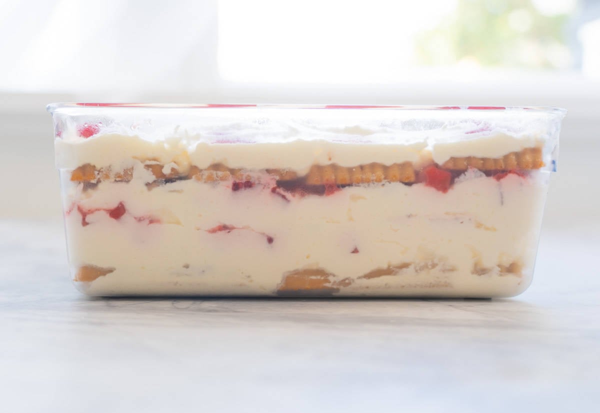 A strawberry shortcake ice box cake in a glass container, the layers of cream cookies and strawberries visible. 