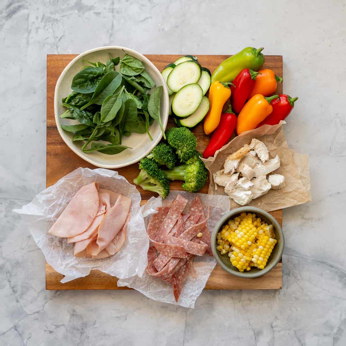 A selection of meats and vegetables laid out on a wooden serving board showing topping ideas