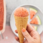 A waffle cone topped with pink sorbet being held up to the camera.
