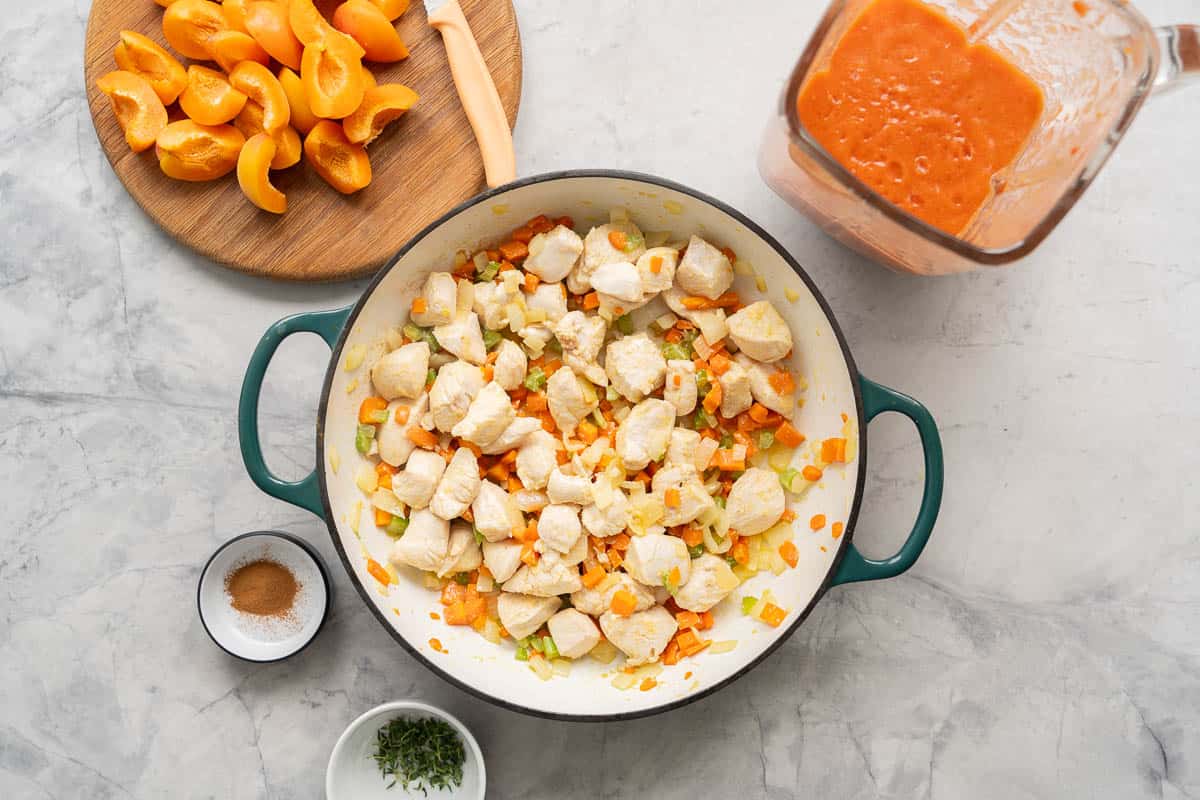 A skillet of sealed chicken, and diced vegetables on a bench top surrounded by more ingredients to make apricot chicken.