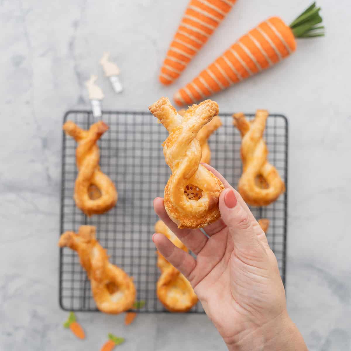 A puff pastry cheese straw twisted into the shape of a bunny being held up to the camera.