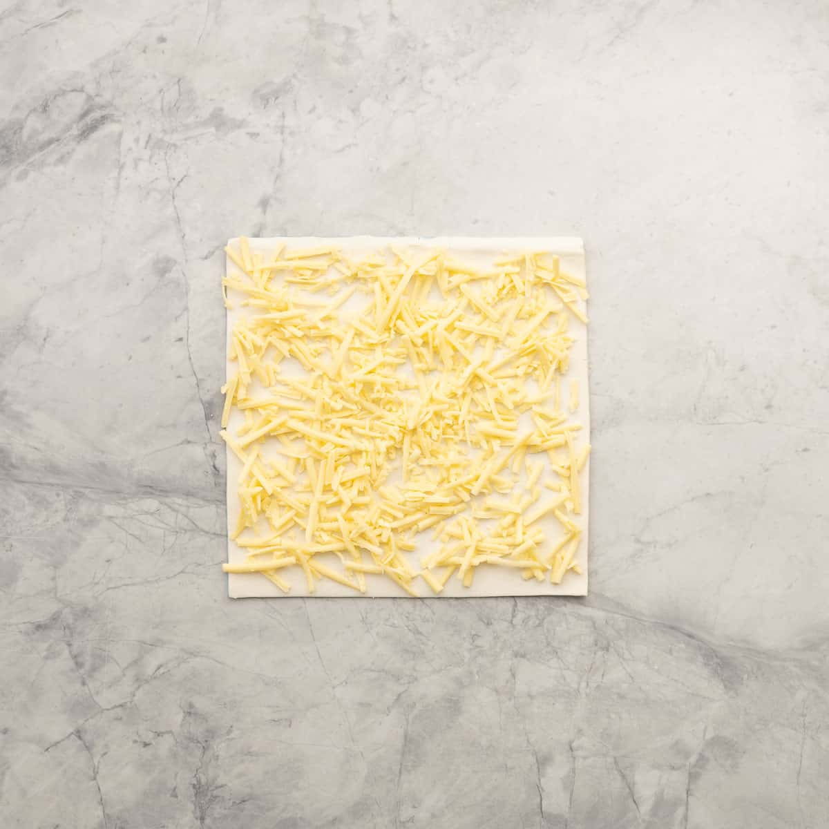 A square sheet of puff pastry covered with a layer of grated cheese. 