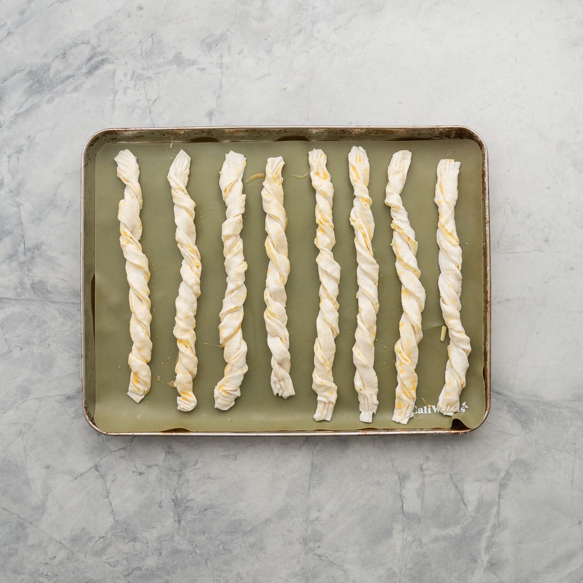 Puff pastry cheese straws on a silicone baking mat ready to go into the oven 