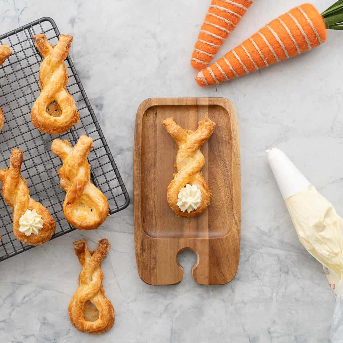 A cheese straw bunny twist on a small wooden serving platter with a cream cheese tail. 