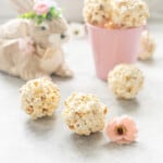 Three tennis ball sized balls of popcorns on a bench infant of a decorative easter bunny and spring flowers.
