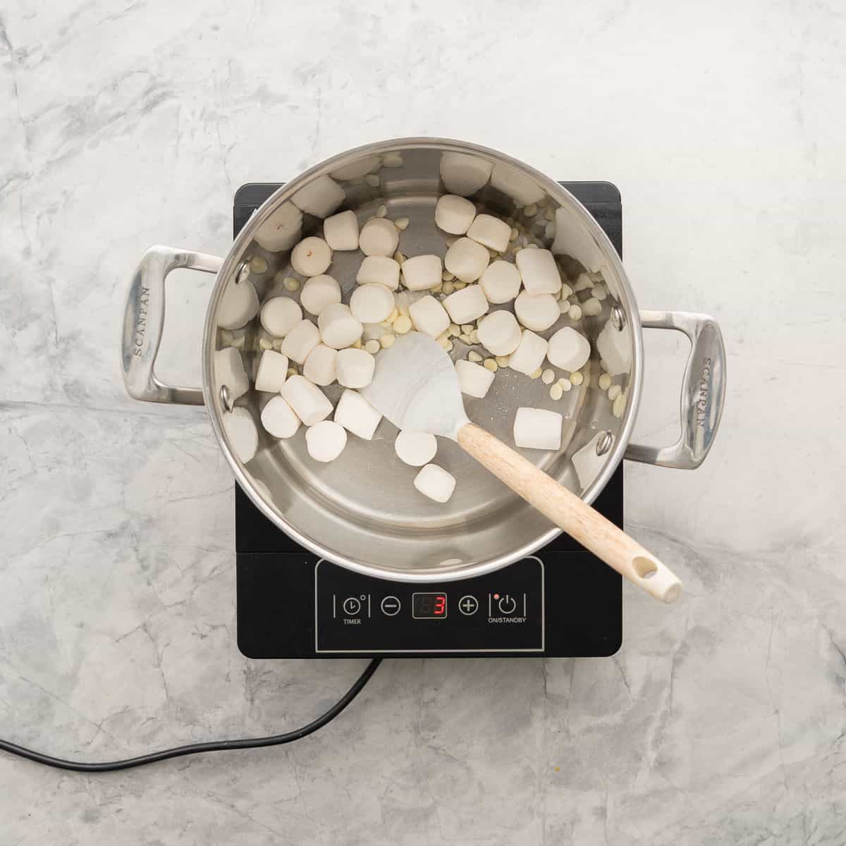 A large sauce pan of marshmallows, white chocolate chips and coconut oil on a portable element. 