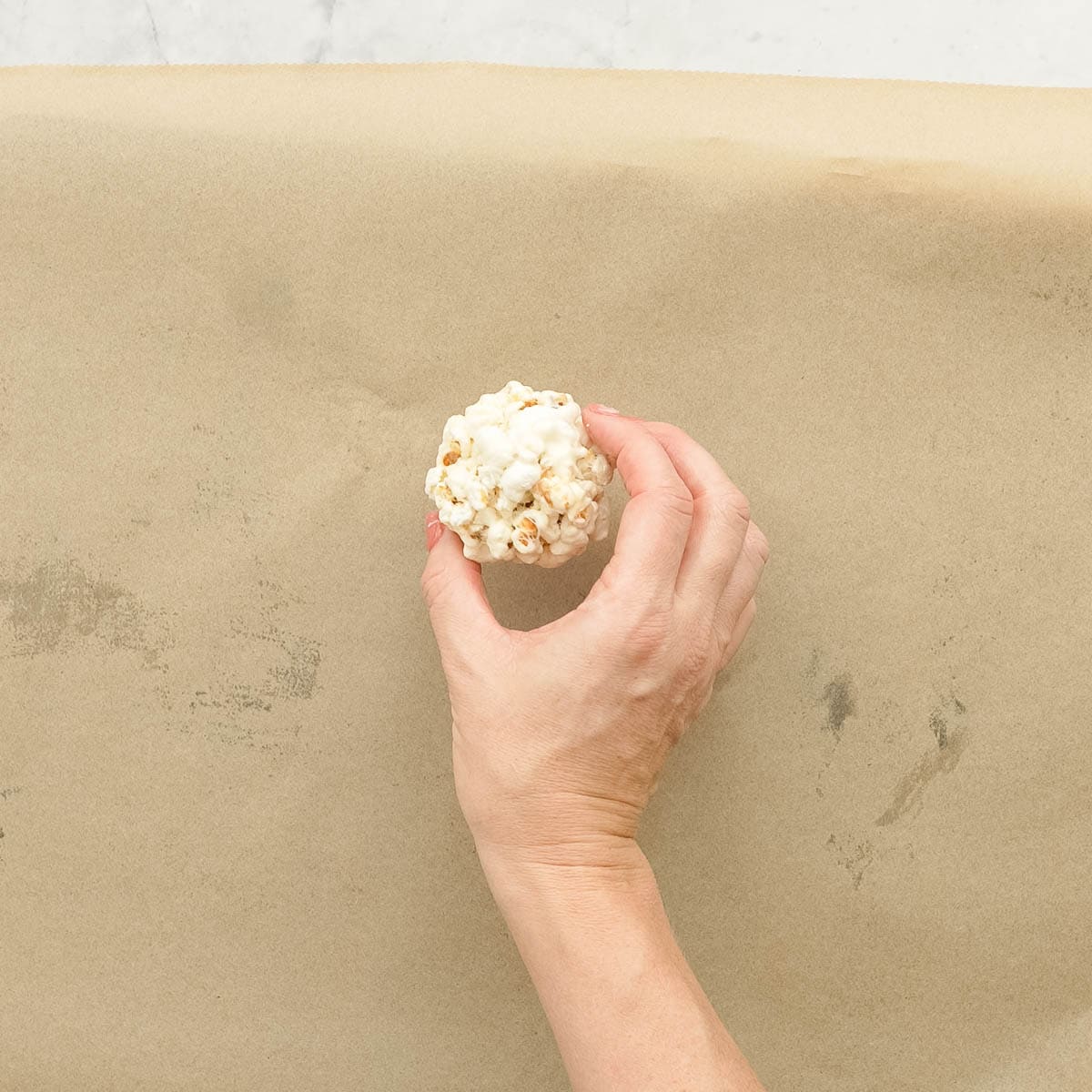 A hand forming a popcorn ball. 