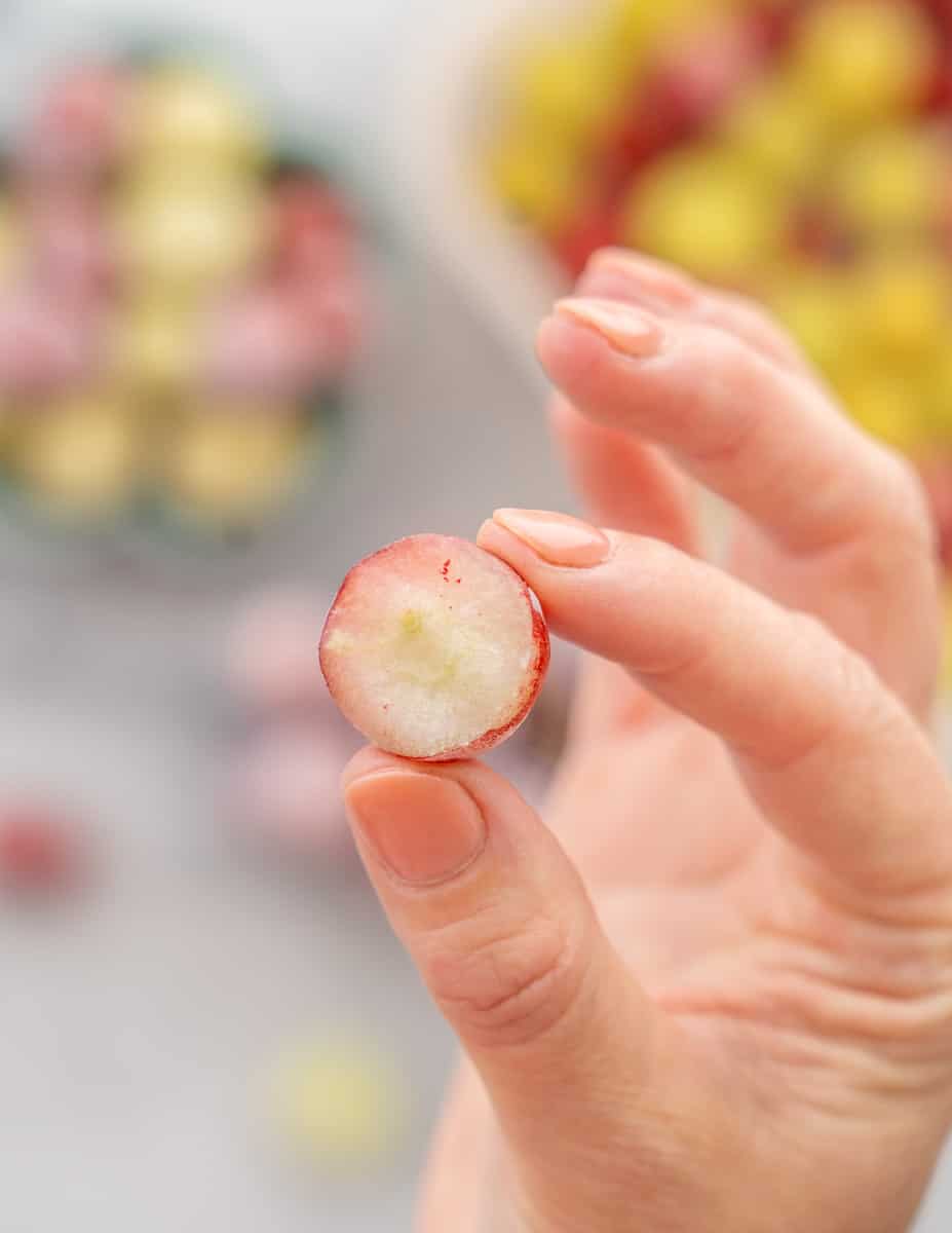 A hand holding up one frozen and sliced red grape.