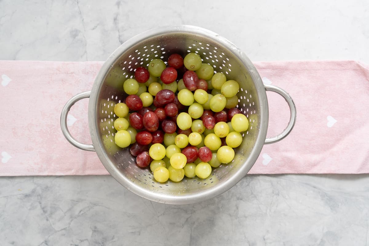 Fresh green and red grapes washed in a colander resting on a tea towel on the bench 