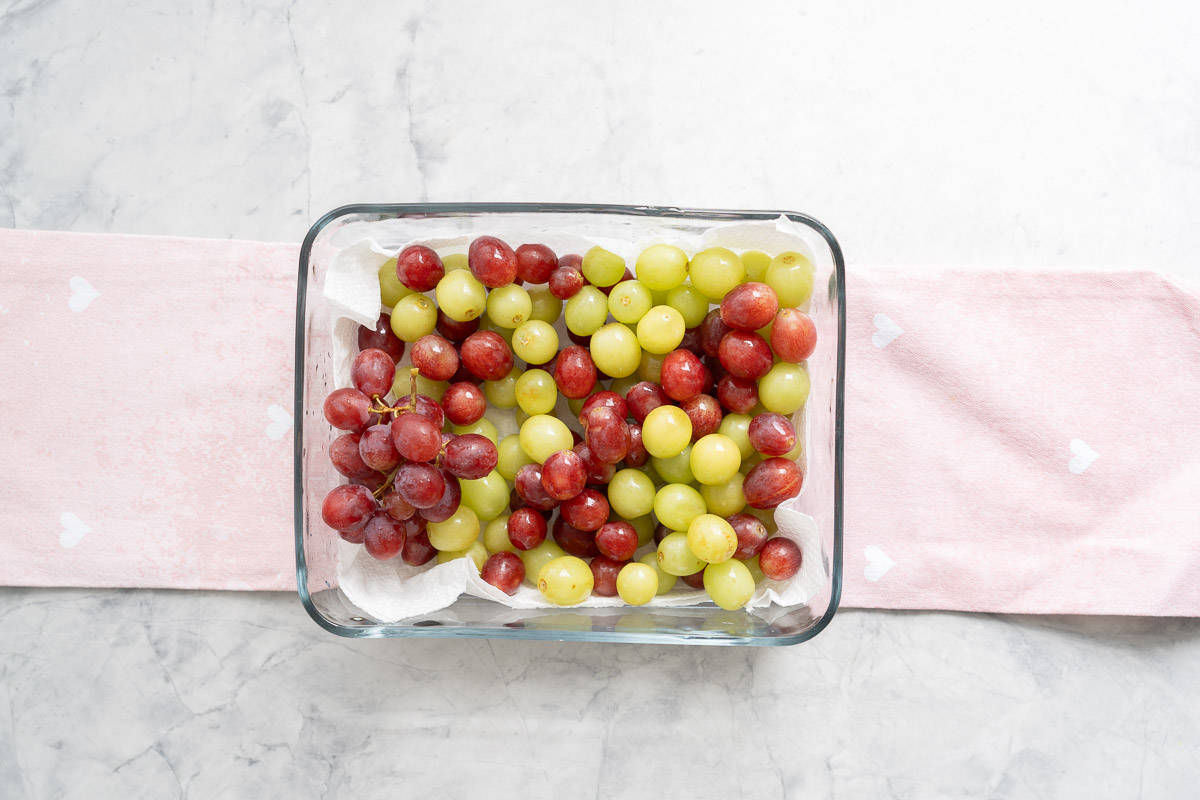 Fresh green and red grapes sitting on a lined glass storage container. 