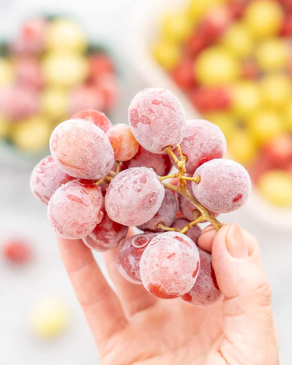 A hand holding up a bunch of red frozen grapes