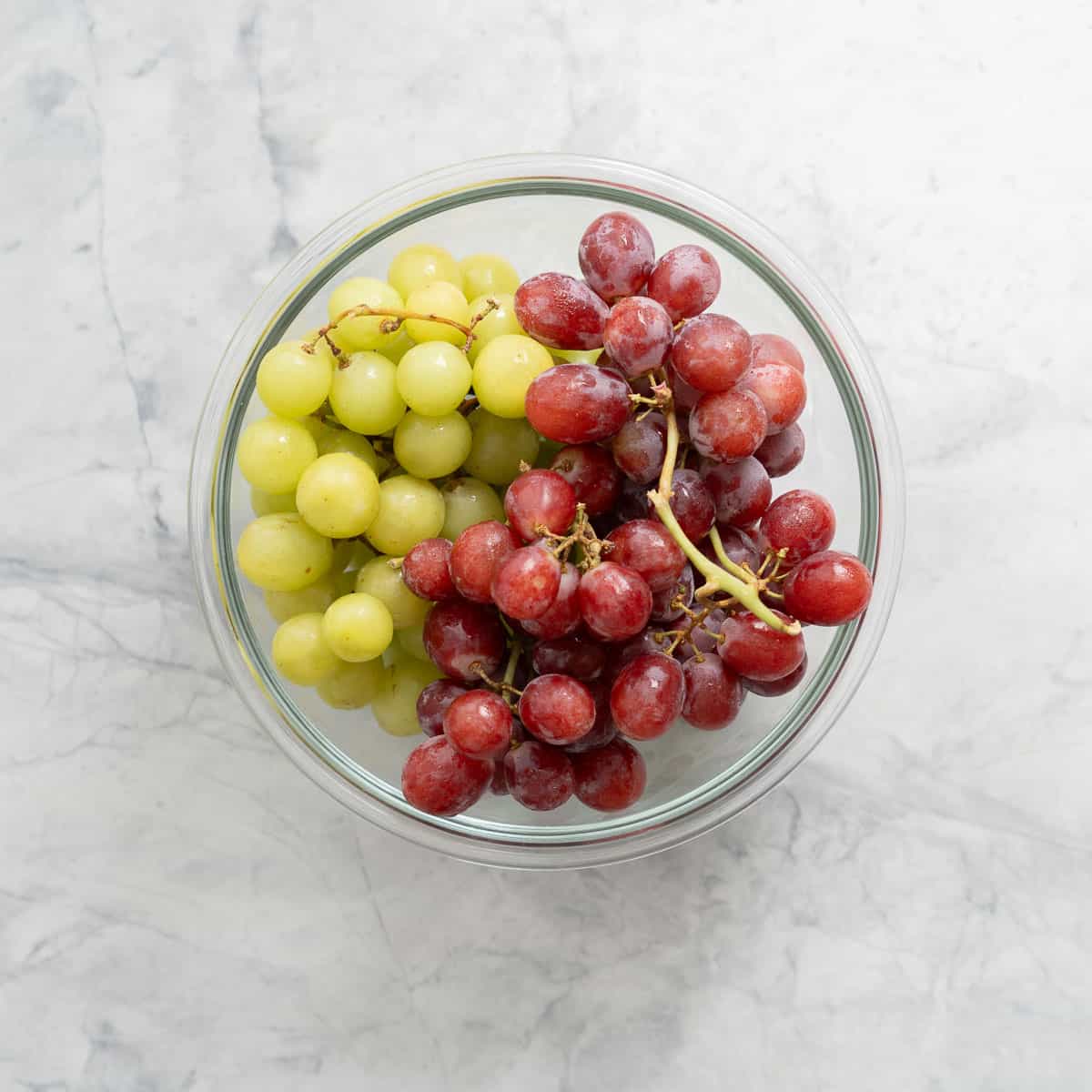 Fresh bunches of green and red grapes in a large glass bowl sitting on the bench 
