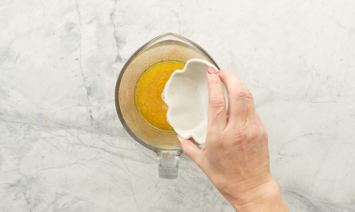 Clear liquid being poured into a glass measuring jug of melted butter. 
