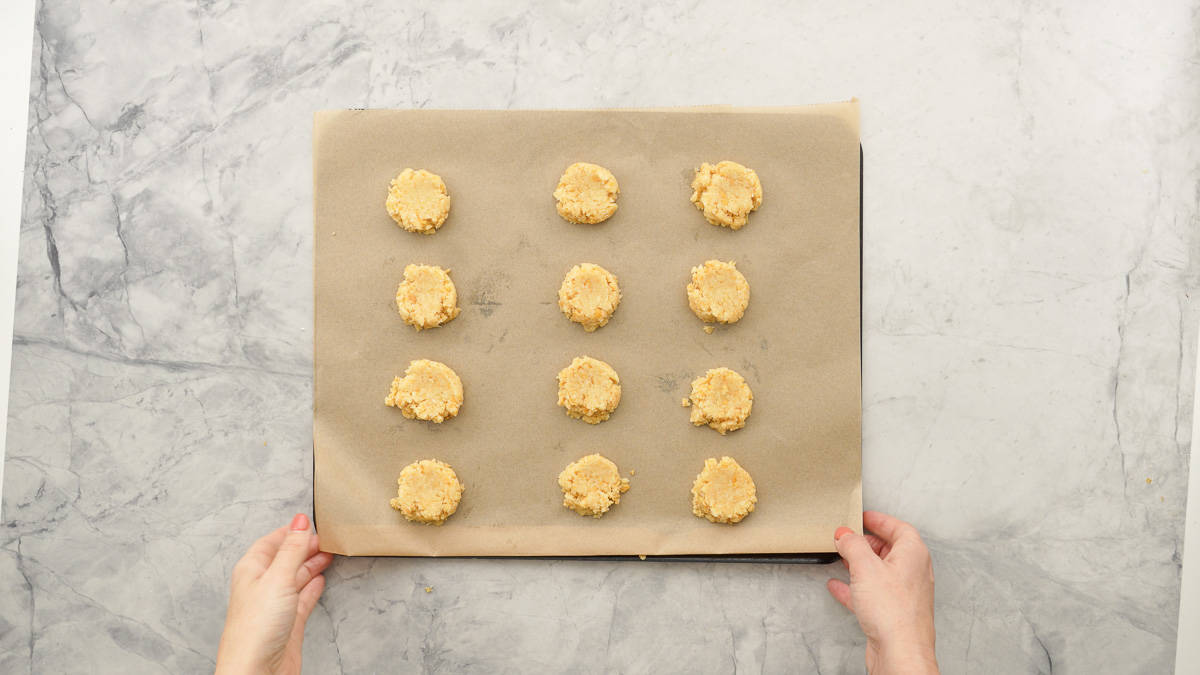 A lined baking sheet with nine flattened discs of cookie dough ready to go into the oven. 