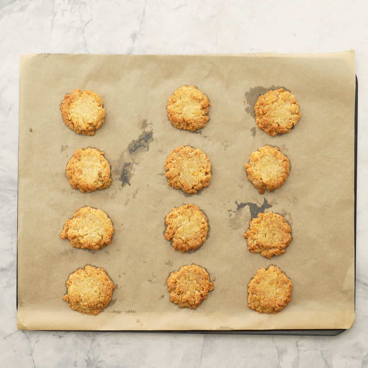 Nine lightly golden Anzac biscuits on a baking paper lined cookie sheet. 