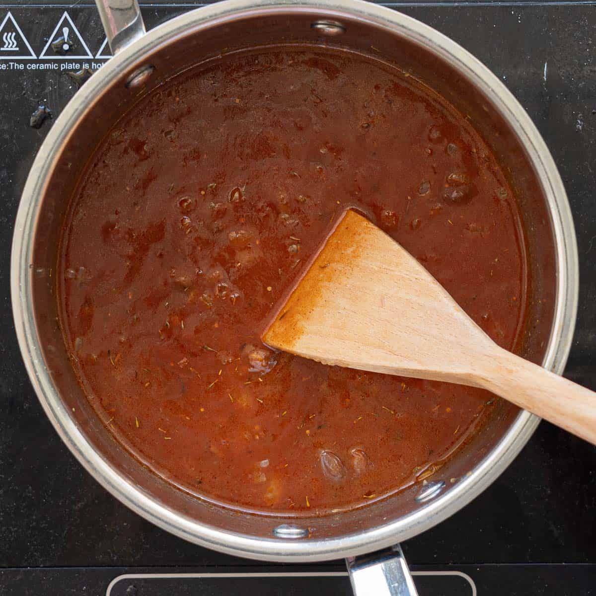 A large saucepan filled with tomato soup, beans visible on the surface of the puree. 
